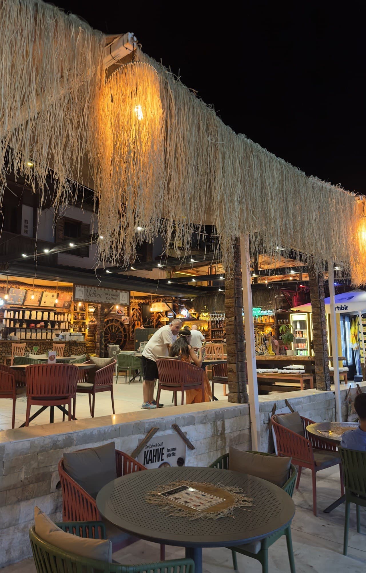 Yelken Cafe Bar gece terası — rafya saçaklı pergola ve sıcak ışıklar